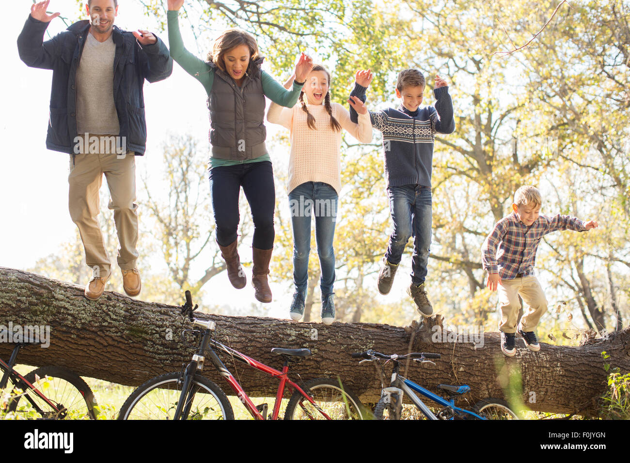 Begeisterte Familie springen von umgestürzten Baumstamm über Fahrräder Stockfoto