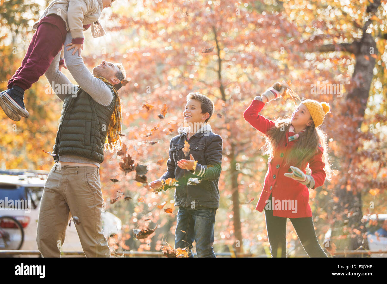 Verspielte Vater und Kinder spielen im Herbstlaub Stockfoto