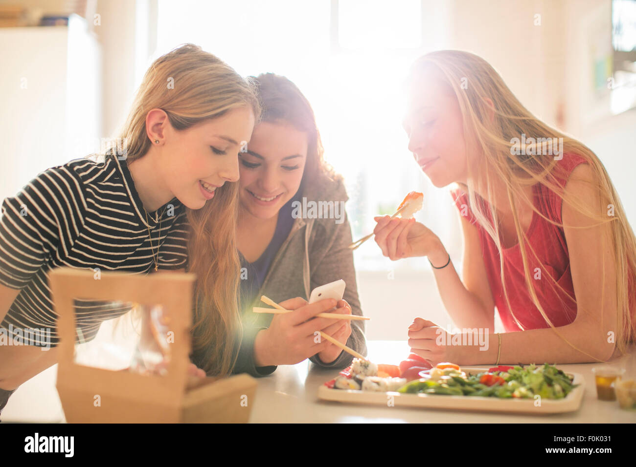 Mädchen im Teenageralter Essen Sushi und SMS mit Handy in sonnige Küche Stockfoto