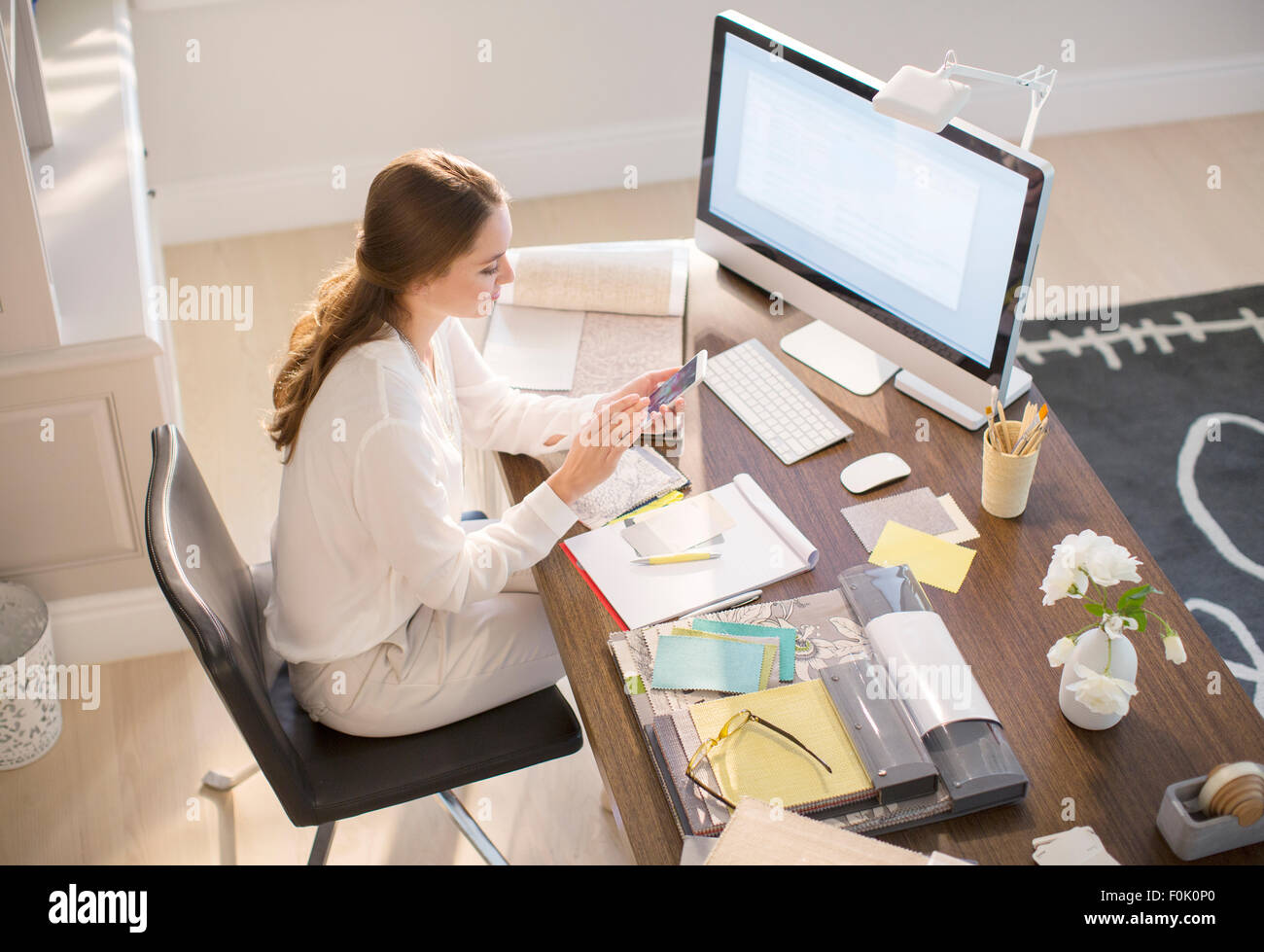 Interior Designer SMS auf Handy am Schreibtisch im home-office Stockfoto