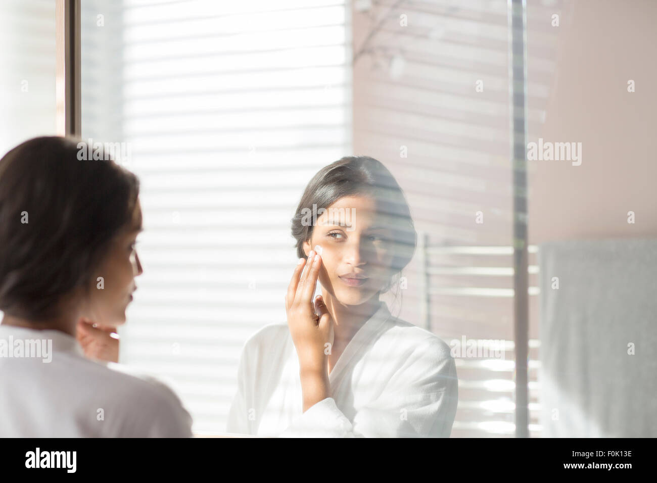 Frau, die Wange im Badezimmerspiegel Feuchtigkeitscreme zuweisen Stockfoto