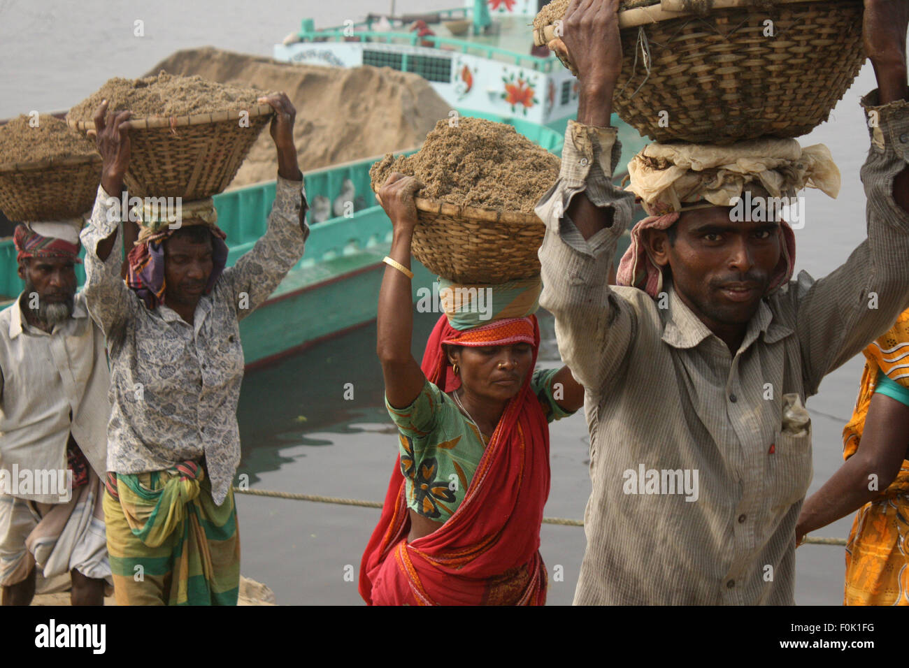 Männliche und weibliche Arbeiter tragen schwere Lasten von Sand auf ihre Köpfe in die Bank von Turag River bei Gabtoli in Dhaka ausgeglichen. Stockfoto