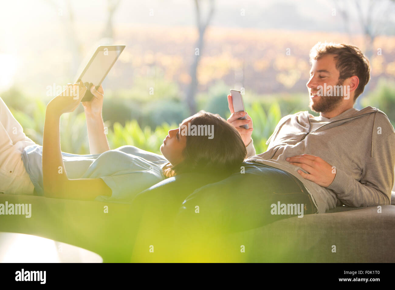 Paar zu verlegen und mit digitalen Tablet und Handy auf sonnigen Terrasse Stockfoto