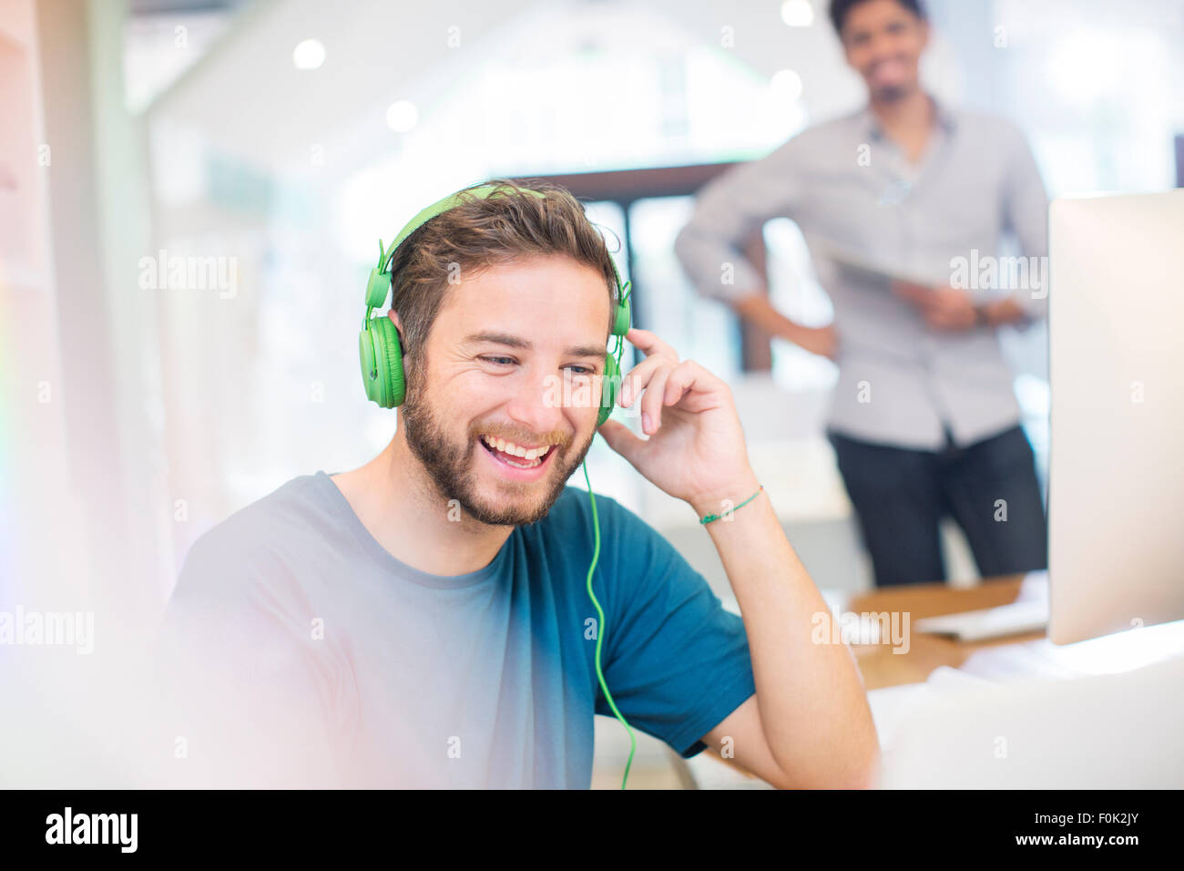 Lächelnde kreative Geschäftsmann hören Kopfhörer im Büro Stockfoto