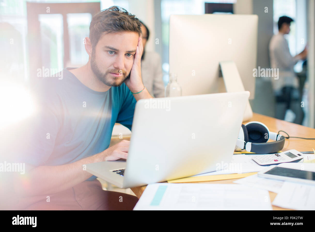 Ernsthafte kreative Geschäftsmann mit Laptop mit Kopf in Händen im Büro Stockfoto