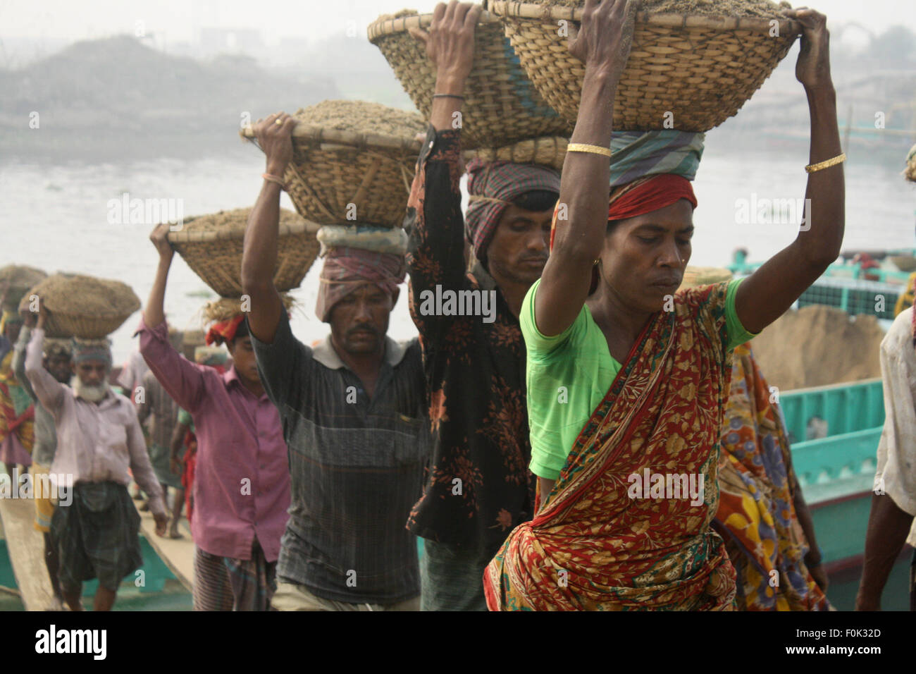 Männliche und weibliche Arbeiter tragen schwere Lasten von Sand auf ihre Köpfe in die Bank von Turag River bei Gabtoli in Dhaka ausgeglichen. Stockfoto