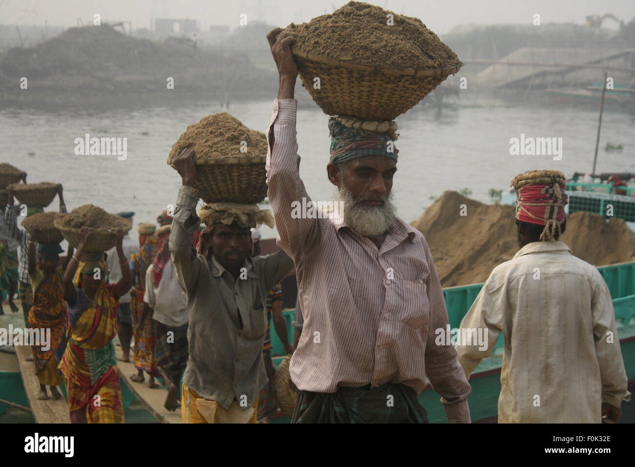 Männliche und weibliche Arbeiter tragen schwere Lasten von Sand auf ihre Köpfe in die Bank von Turag River bei Gabtoli in Dhaka ausgeglichen. Stockfoto