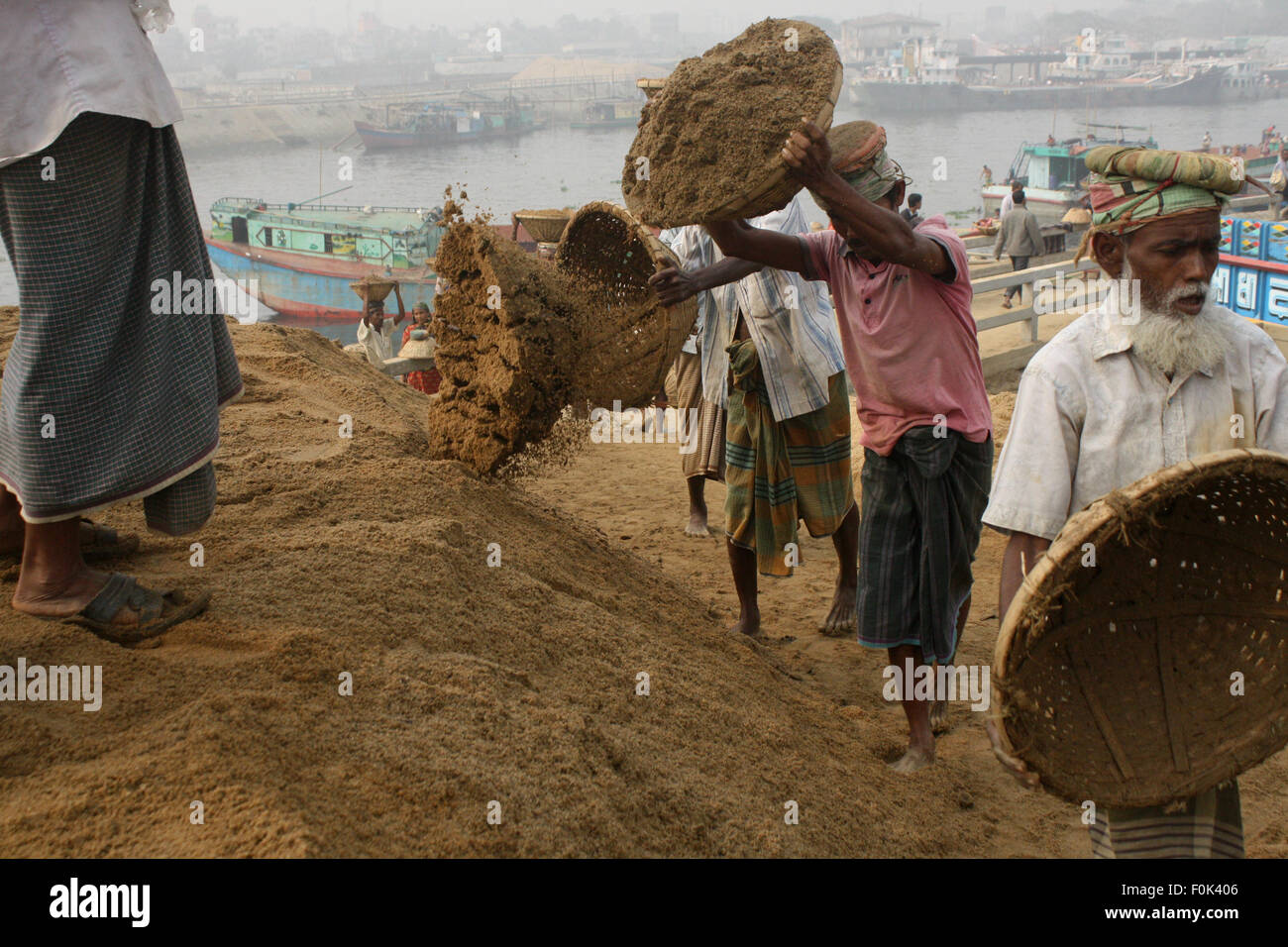 Männliche und weibliche Arbeiter tragen schwere Lasten von Sand auf ihre Köpfe in die Bank von Turag River bei Gabtoli in Dhaka ausgeglichen. Stockfoto