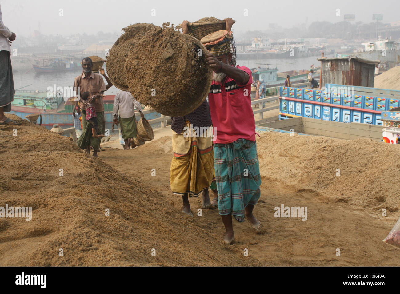 Männliche und weibliche Arbeiter tragen schwere Lasten von Sand auf ihre Köpfe in die Bank von Turag River bei Gabtoli in Dhaka ausgeglichen. Stockfoto