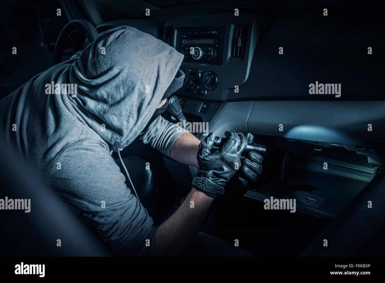 Auto-Rubber im Auto. Kautschuk mit Taschenlampe, die auf der Suche nach Wertsachen im Auto. Stockfoto