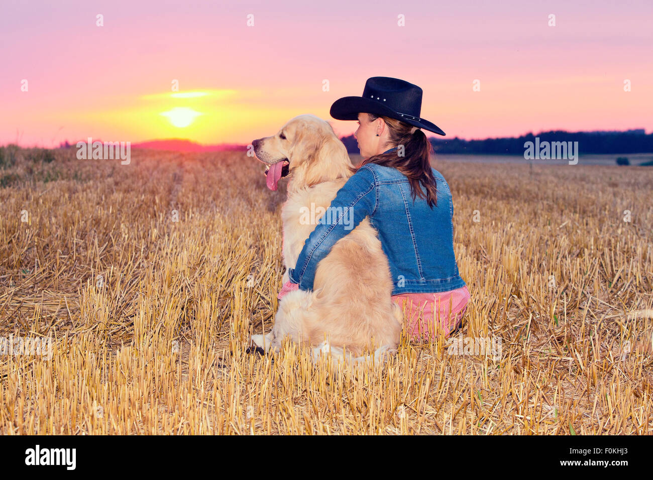Junge Frau mit Golden Retriever sitzend auf Stoppelfeld bei Dämmerung Stockfoto