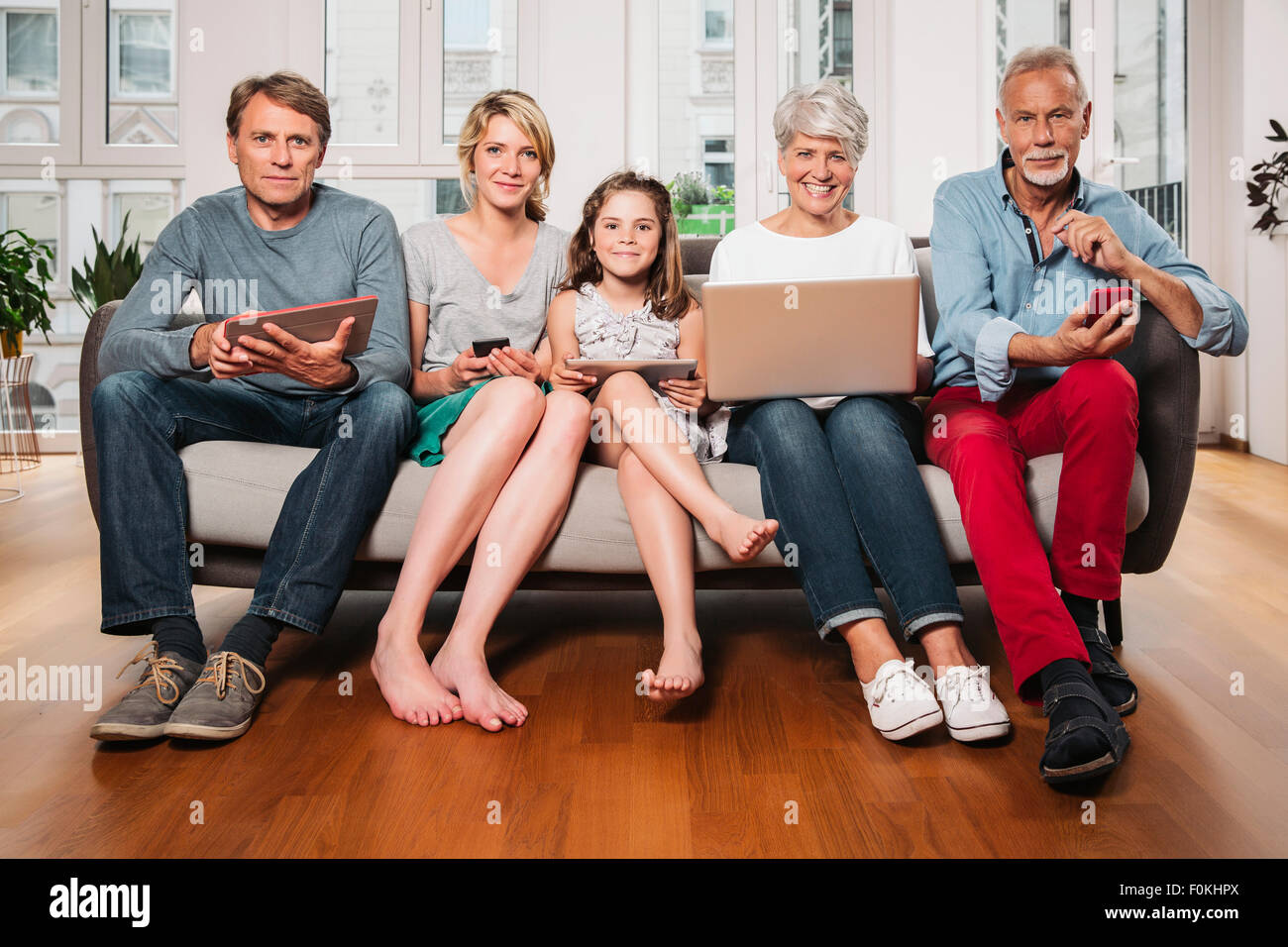 Gruppenbild der drei-Generationen-Familie mit verschiedenen digitalen Geräten sitzen auf einer couch Stockfoto