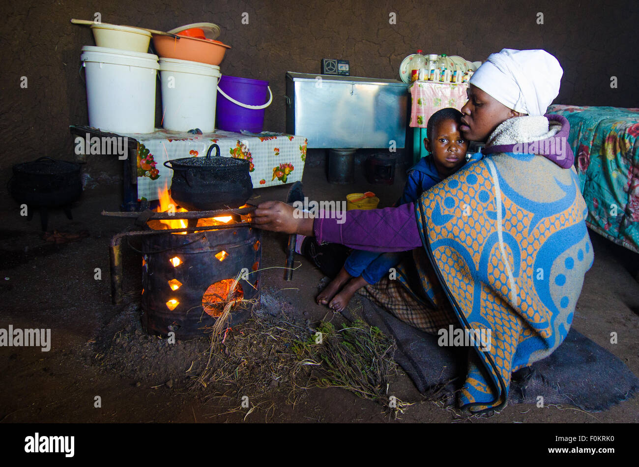 Ein Kind schaut neugierig zu, wie seine Mutter Essen über eine kleine Feuerstelle in einem ländlichen Basotho nach Hause kocht. Stockfoto