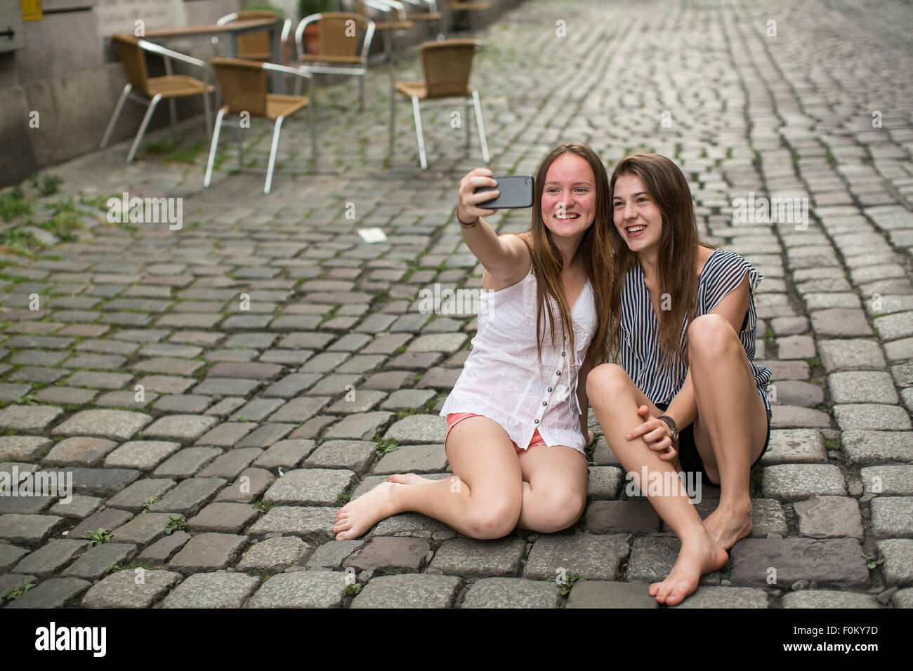 Zwei lustige Mädchen im Teenageralter machst Selfie am Telefon sitzt auf dem Bürgersteig. Stockfoto