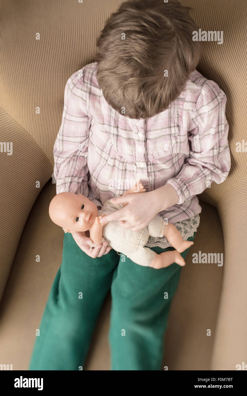 Porträt des kleinen Mädchens Plastikpuppe in ihren Händen hält. Sie sitzt in einem Sessel. Stockfoto