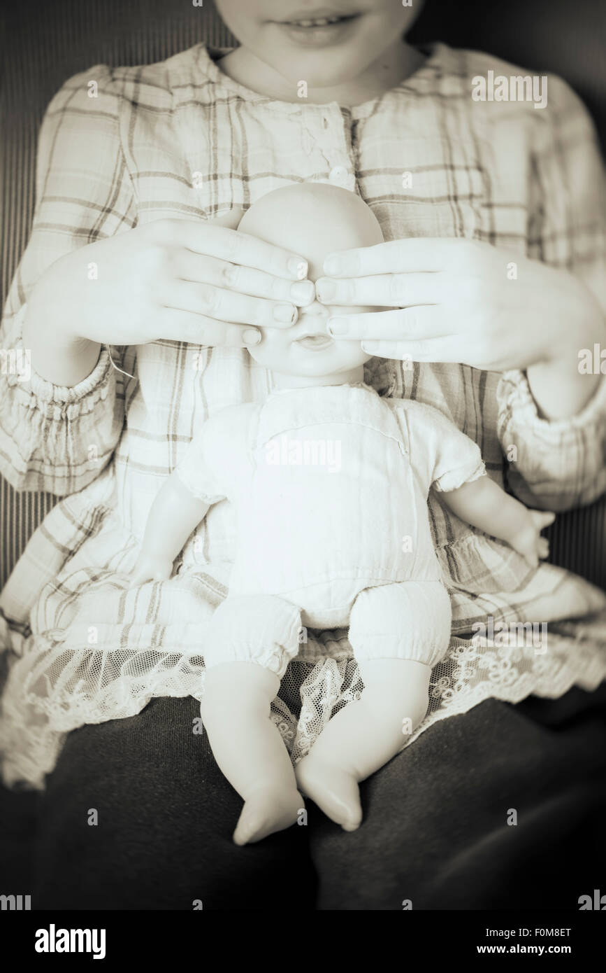 Porträt des kleinen Mädchens Plastikpuppe in ihren Händen hält. Sie deckt die Augen der Puppe spielen Peekaboo. Stockfoto