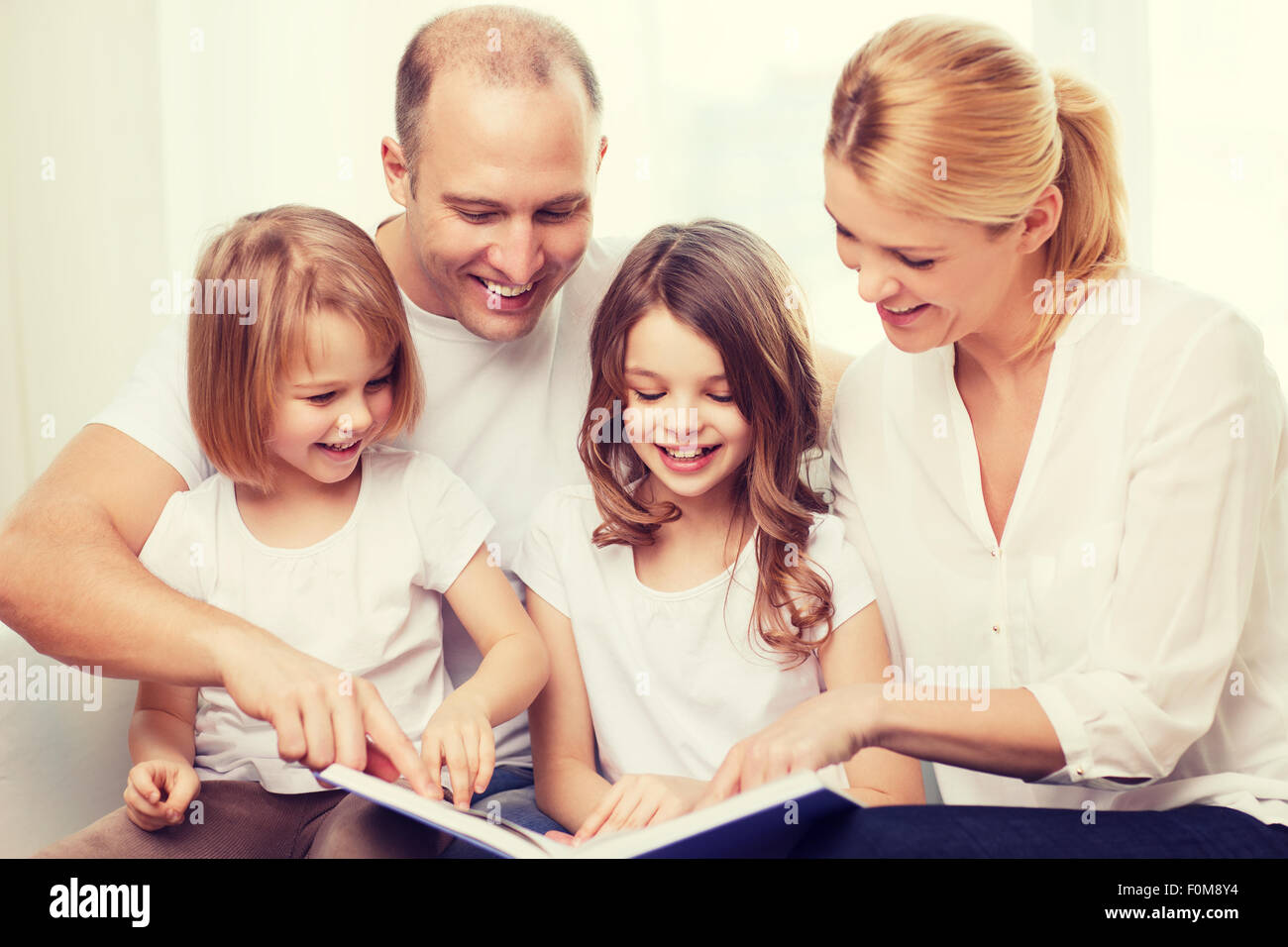 lächelnde Familie und zwei kleine Mädchen mit Buch Stockfoto