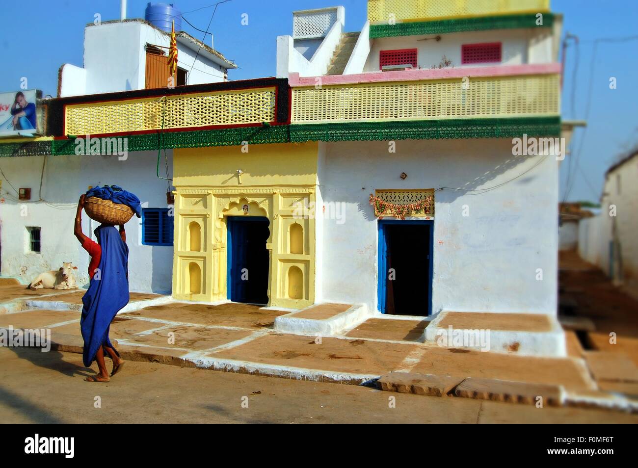 Frau in blau mit einem Korb auf dem Kopf in einer ruhigen Straße im Dorf Orchha, Madhya Pradesh, Indien Stockfoto