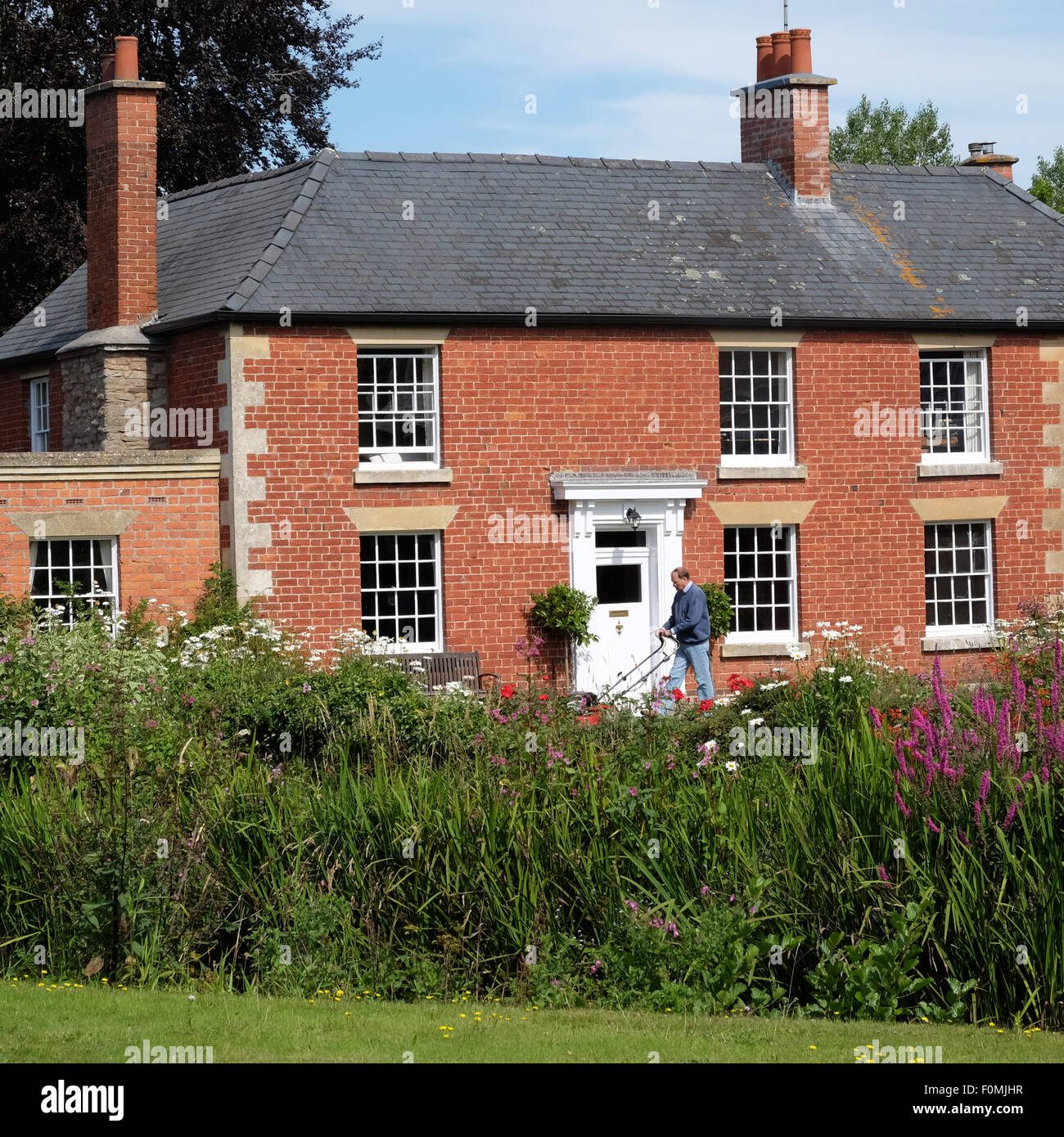 Eardisland Herefordshire Mann mäht Rasen Rasen in eleganten alten Gebäude aus rotem Backstein UK Stockfoto