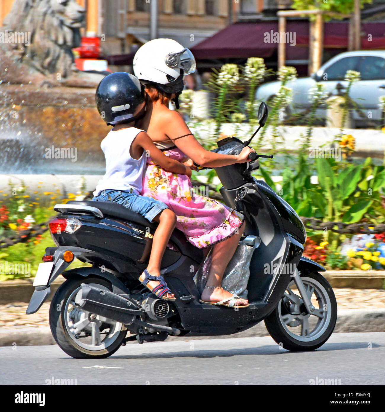Frau Motorroller Fahrer mit kleinen Kind reiten Sozius an einem heißen Sommertag in Aix-En-Provence (verdeckt Nummernschild) Stockfoto