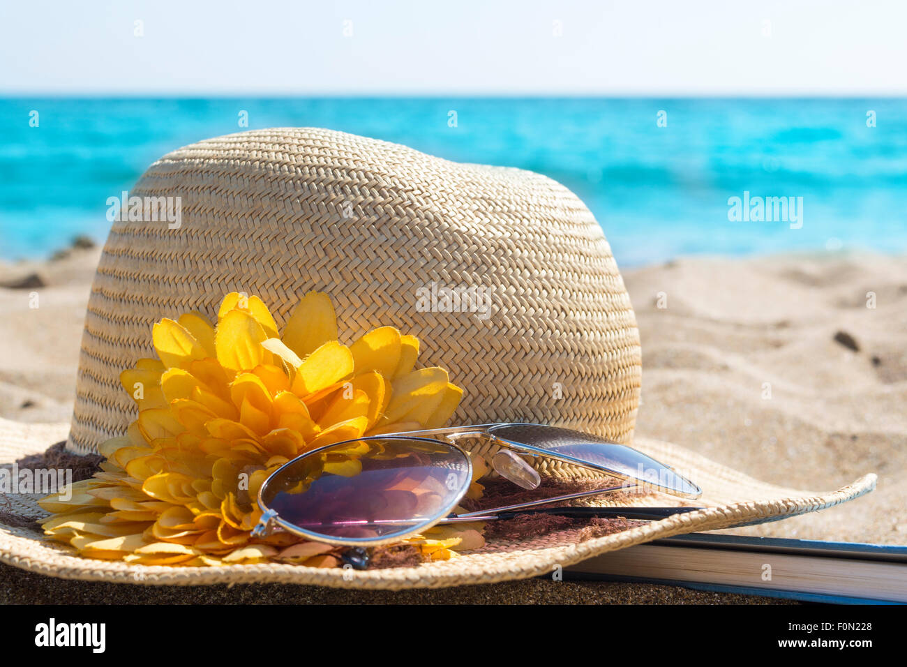 Strohhüte, Sonnenbrille und ein Buch am Strand Stockfoto