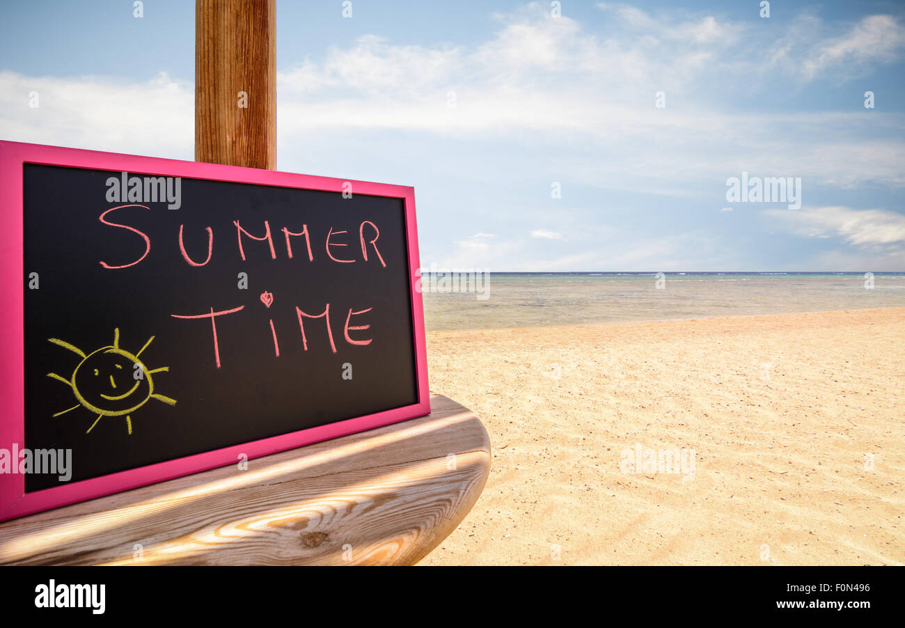 Auf dem Bild einen Sonnenschirm ist die kleine Tafel mit den Worten "Sommerzeit" in einem Strand am Nachmittag. Stockfoto