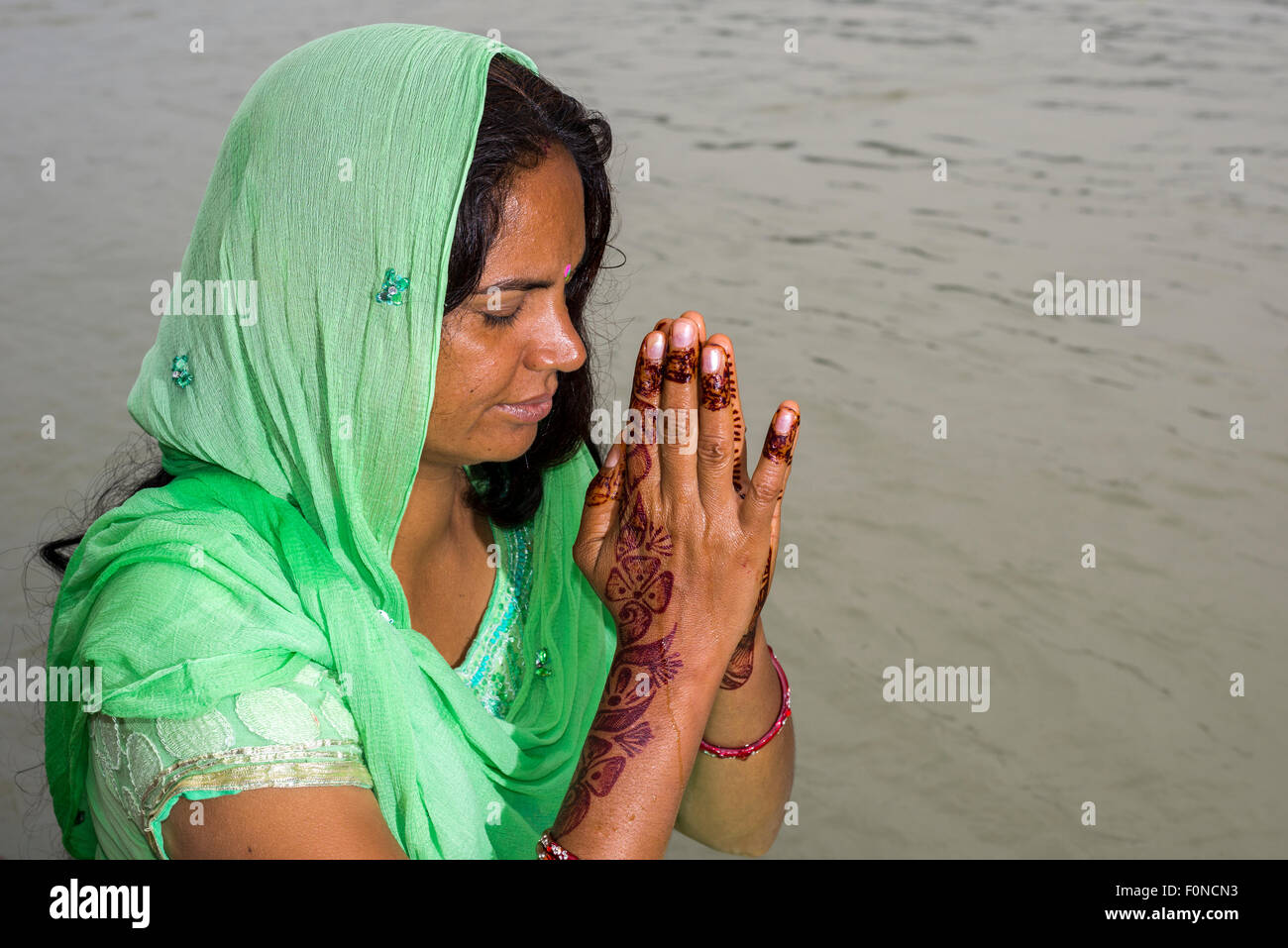 Eine junge Frau mit langen schwarzen Haaren, Henna bemalte Hände und ein grünes Kleid ist an den Ghats von dem heiligen Fluss Ganges beten. Stockfoto