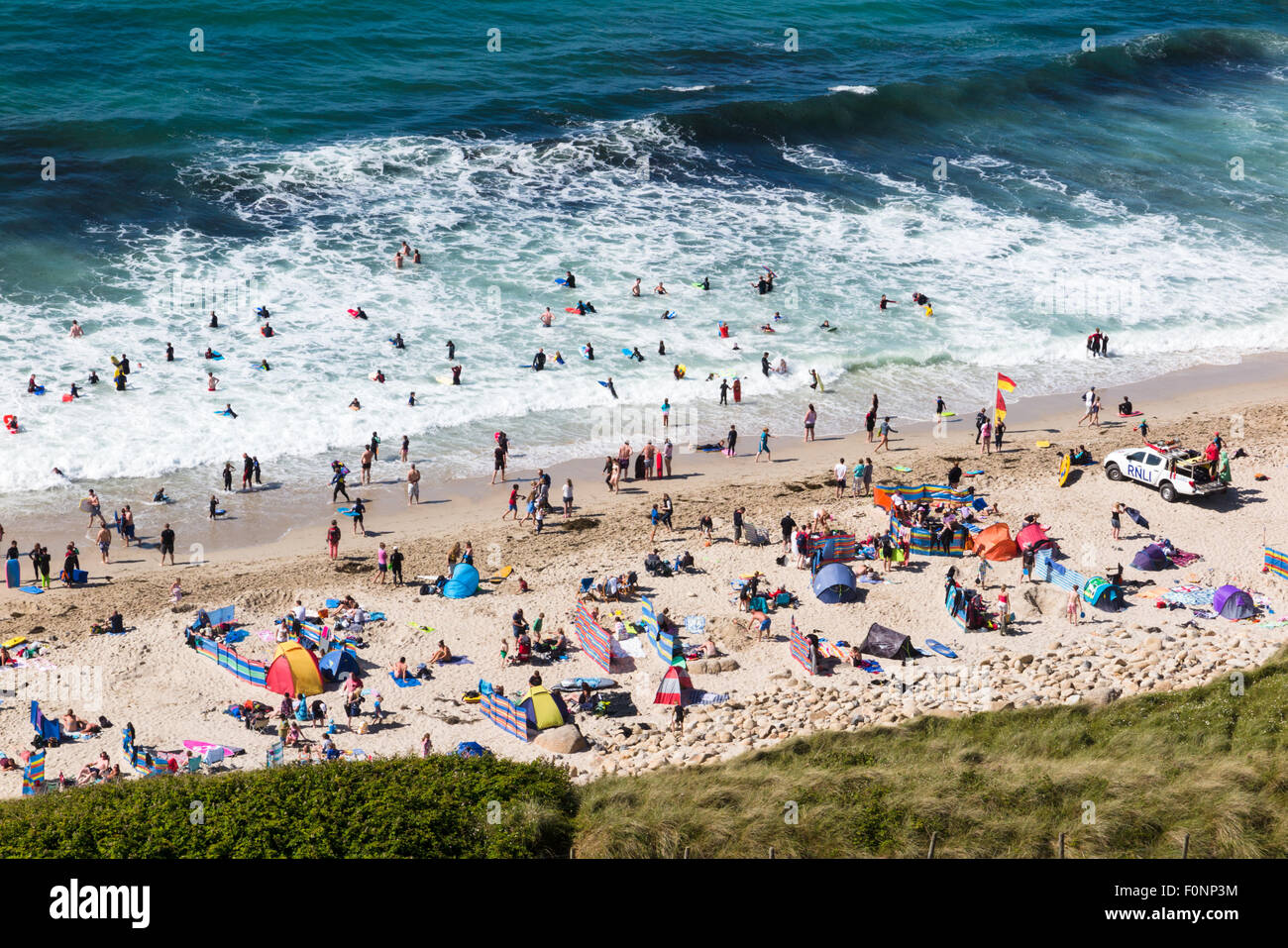Einem anstrengenden Nachmittag auf Sennen Beach in Cornwall. Sonnenanbeter, Surfer und Body Boarder genießen Sie die Sonne und Wellen bei diesem pop Stockfoto
