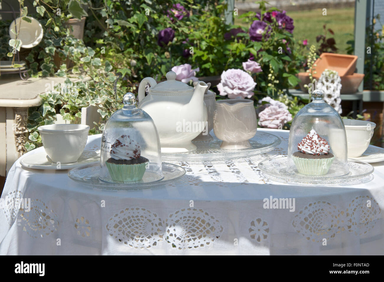 Tee und Kuchen angelegt, auf einem Tisch mit einem weißen Tuch, in einem Garten. Stockfoto