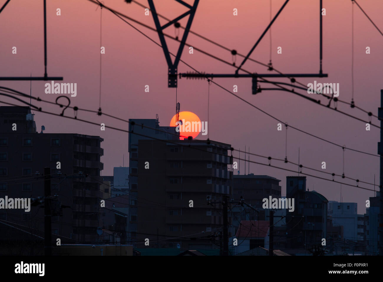 Japan. Sunrise, Sunup. Apartment Blocks und Fahrleitung, die Hochbahn elektrische Leitungen mit einem rötlich dunklen Himmel und ein gelb orange Sonne. Stockfoto