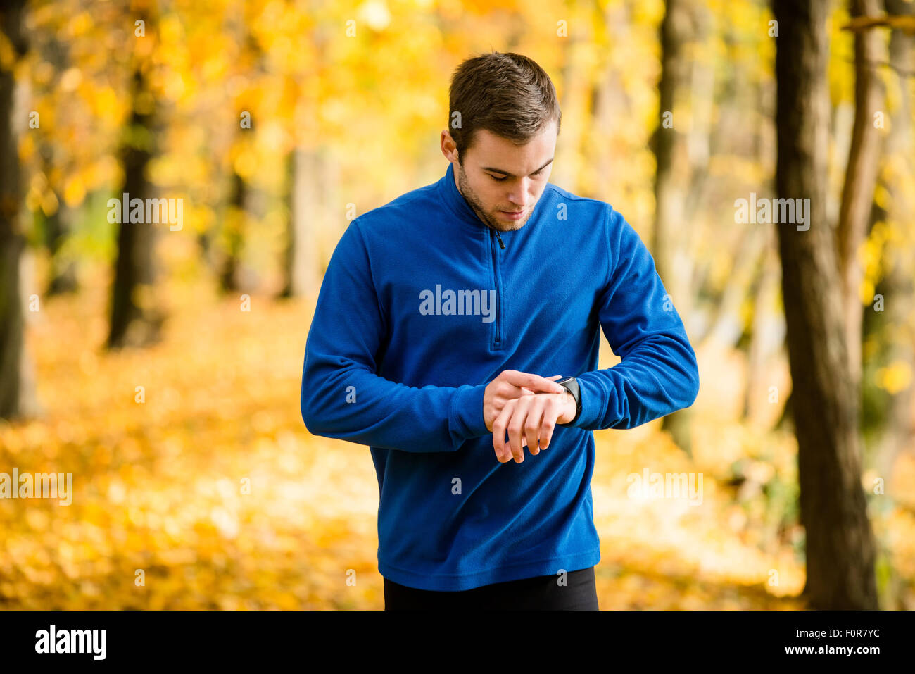 Junger Mann im schönen Herbst Natur joggen und Puls Uhren überprüfen Stockfoto