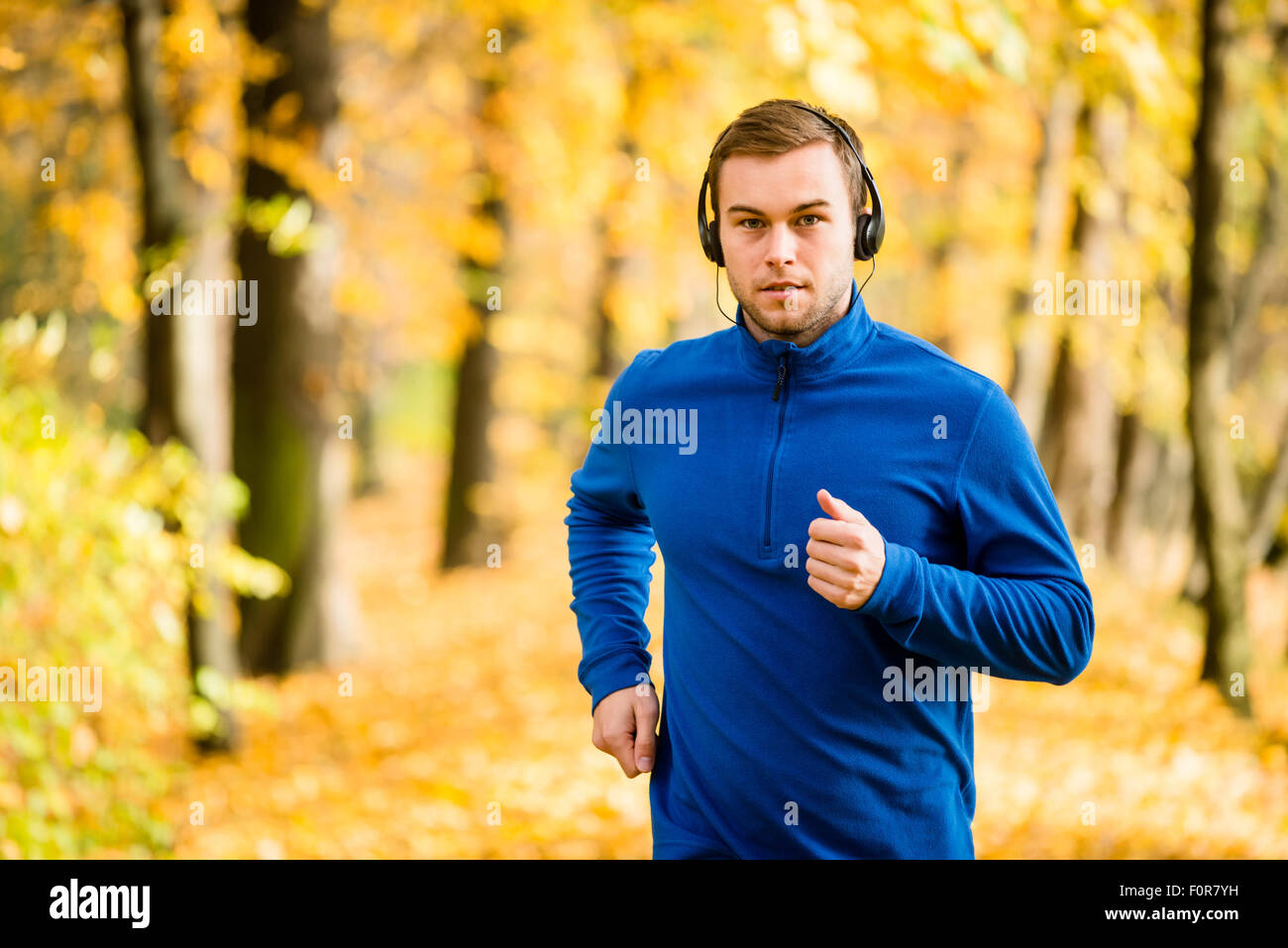 Junger Mann mit Kopfhörern in der herbstlichen Natur joggen und Musik hören Stockfoto