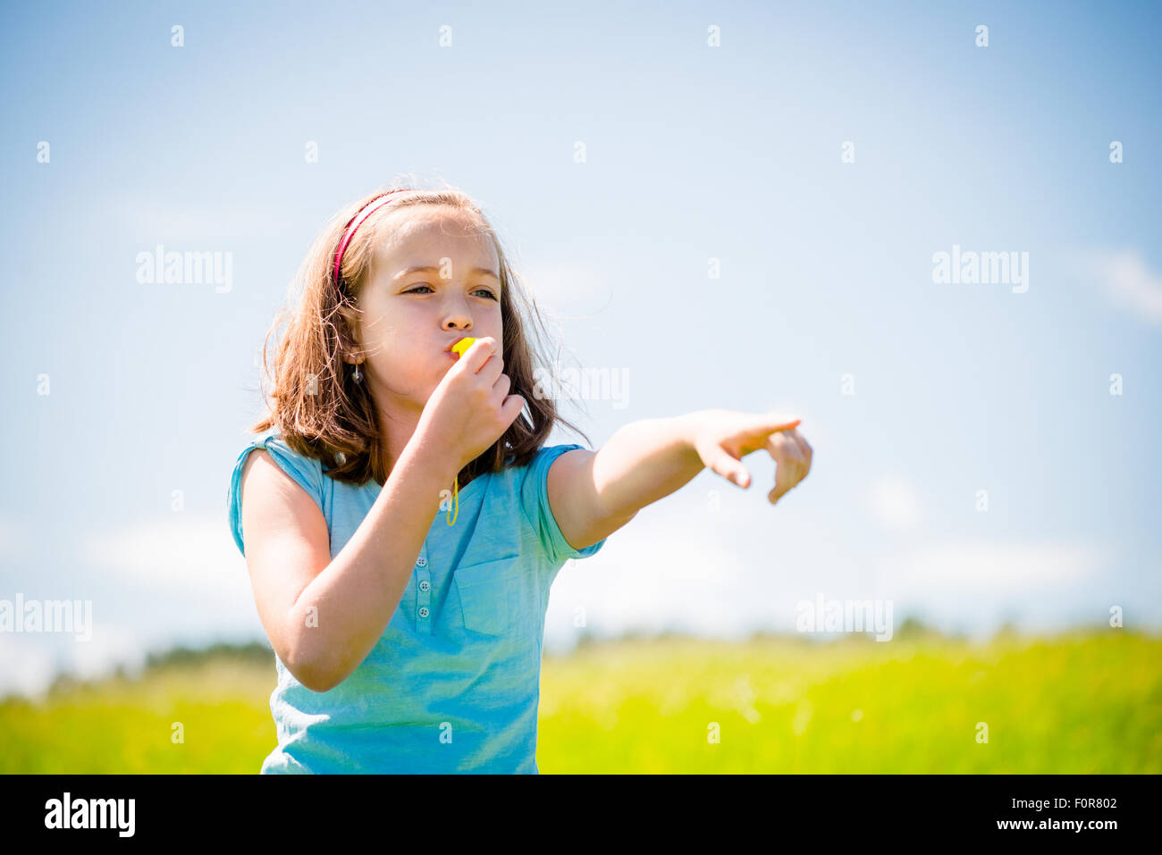 Cute Teen Mädchen weht in Pfeifen und zeigen mit Hand - im Freien in der Natur Stockfoto