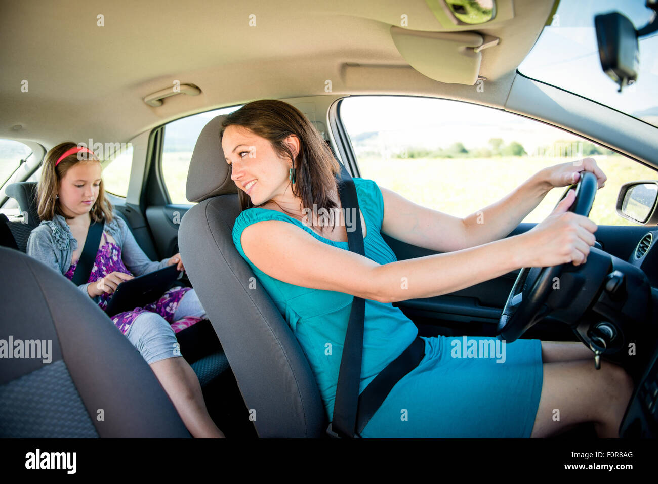 Mutter fährt Auto und Kind sitzt auf dem Rücksitz, Frau kehrt Stockfoto