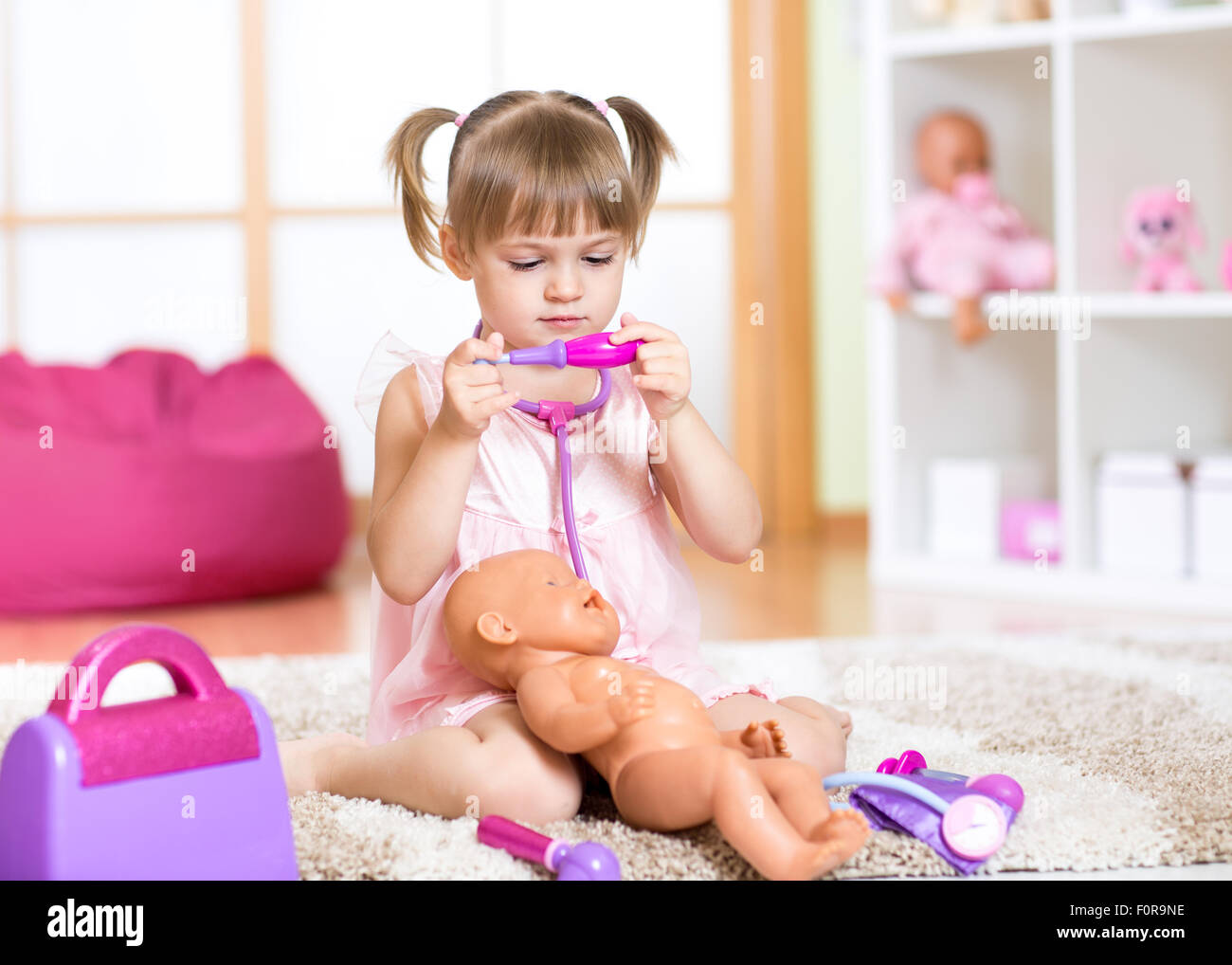 Kind Mädchen spielt des Arztes mit seiner Puppe neugeborenes Baby im Zimmer Stockfoto