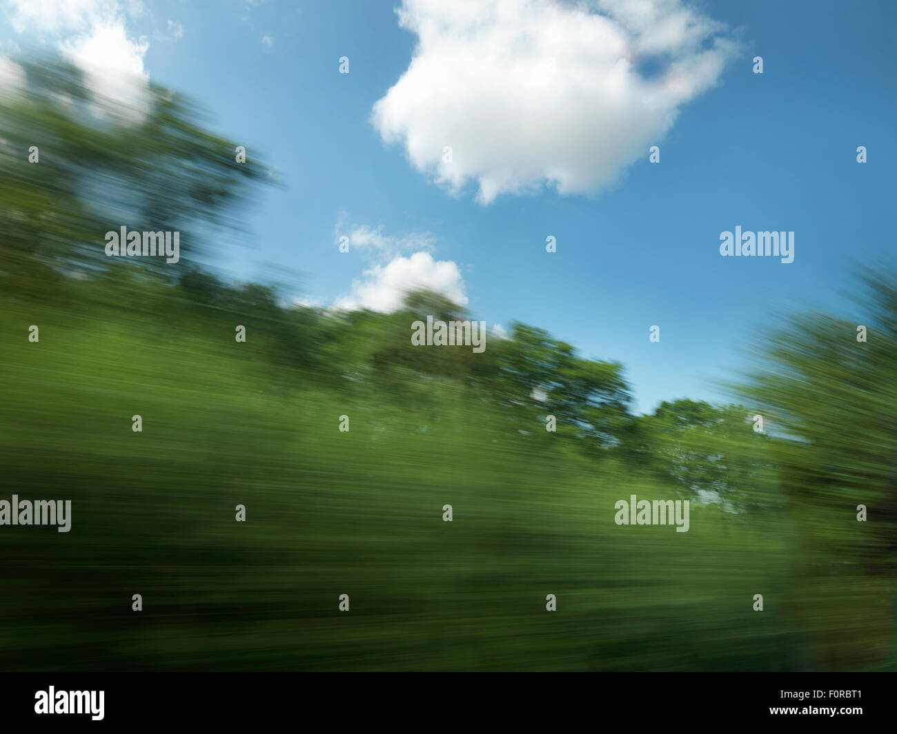 Schuss aus einem Fenster von einem schnell fahrenden Zug verschwommene Bäume und die Landschaft mit blauem Himmel an einem hellen Sommertag. Stockfoto