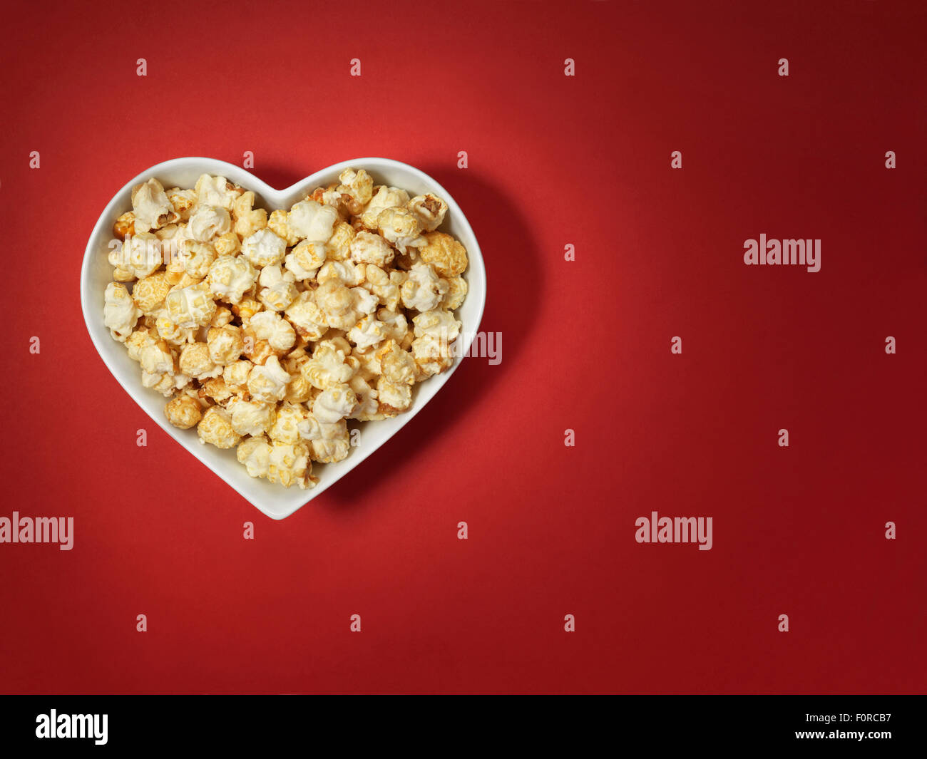 Schuss von Kino Stil Popcorn in ein Herz geformt Schüssel auf einem leuchtend roten Hintergrund mit vielfarbig, Vignette Beleuchtung und offset Stockfoto