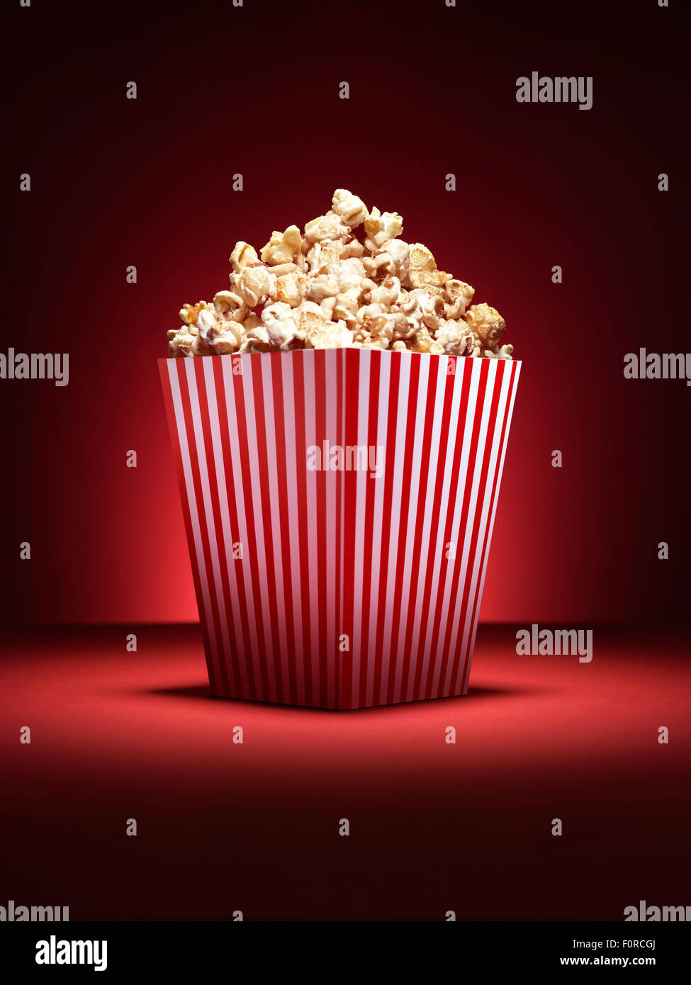 Aufnahme einer traditionellen Box Kino Stil Popcorn mit Anstrahlung auf einem pulsierenden roten Hintergrund mit textfreiraum für den designer Stockfoto