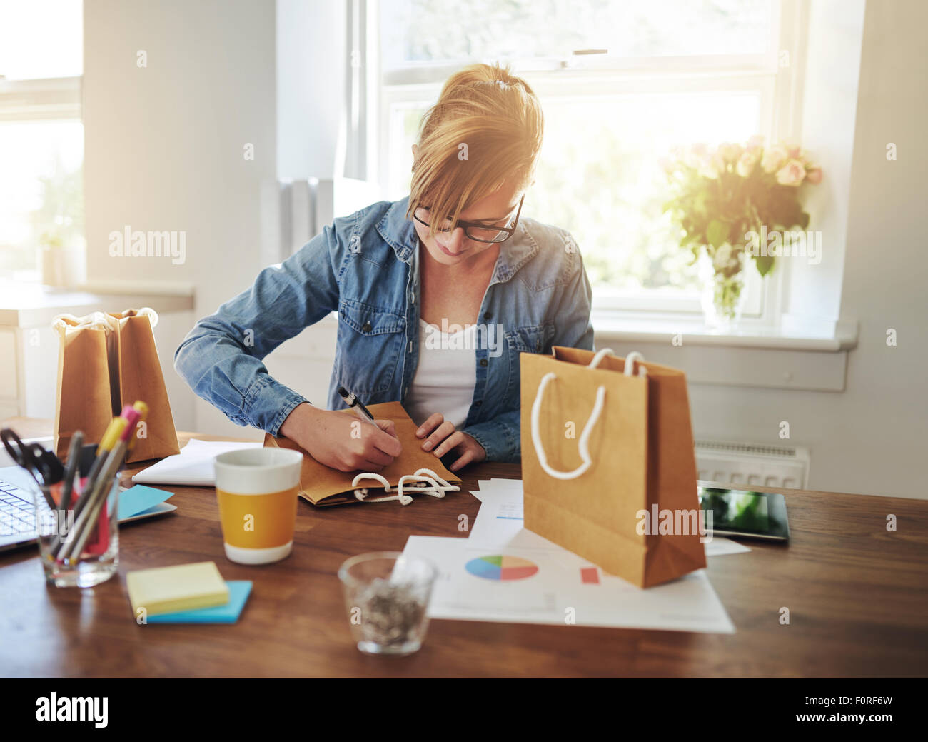 Junge Geschäftsfrau, die Gestaltung von Verpackungen für ihre neue Start-up Online-Geschäft sitzt an ihrem Schreibtisch zu Hause arbeiten auf eine Geschenktüte Stockfoto
