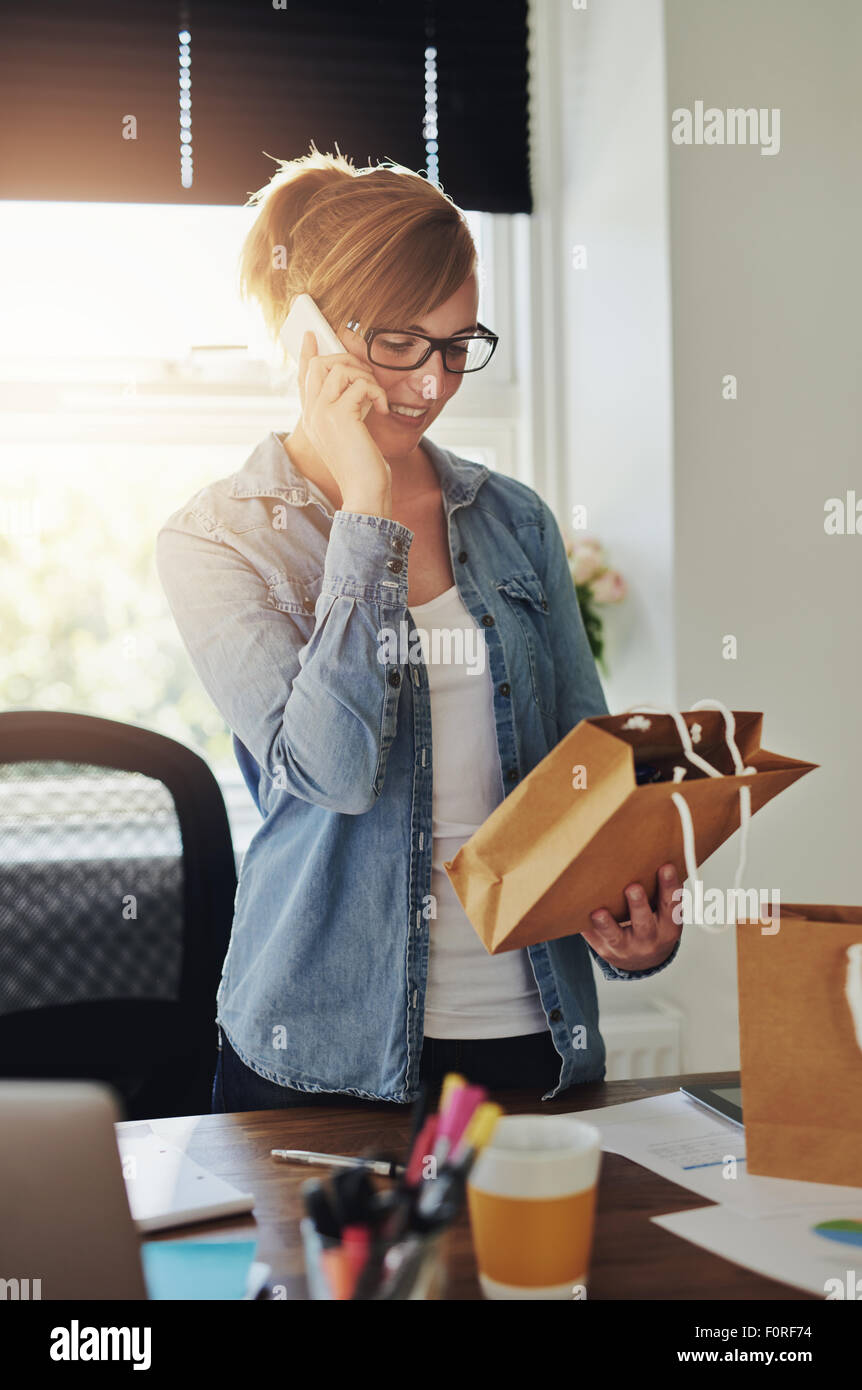 Lächelnd attraktive junge weibliche Unternehmer stehen in Ihrem Home Office unter Bestellungen, die über das Telefon für Produkte geworben Stockfoto