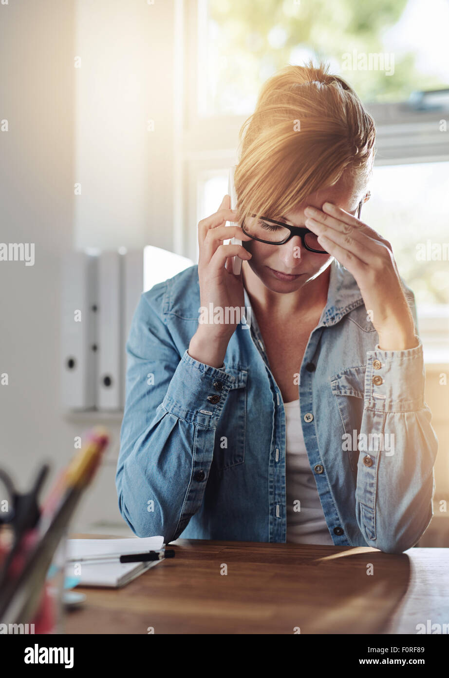 Betroffenen Unternehmerin auf einem Telefon zu sprechen, als sie an ihrem Schreibtisch sitzt in ihrem Büro zu Hause mit ihrem Kopf in die hand Stockfoto