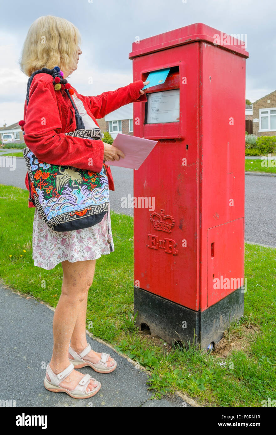 Ältere Frau mailing einen Brief in einen roten rechteckigen Briefkasten in England, Großbritannien, Posten Briefe. Buchen einen Brief. Stockfoto