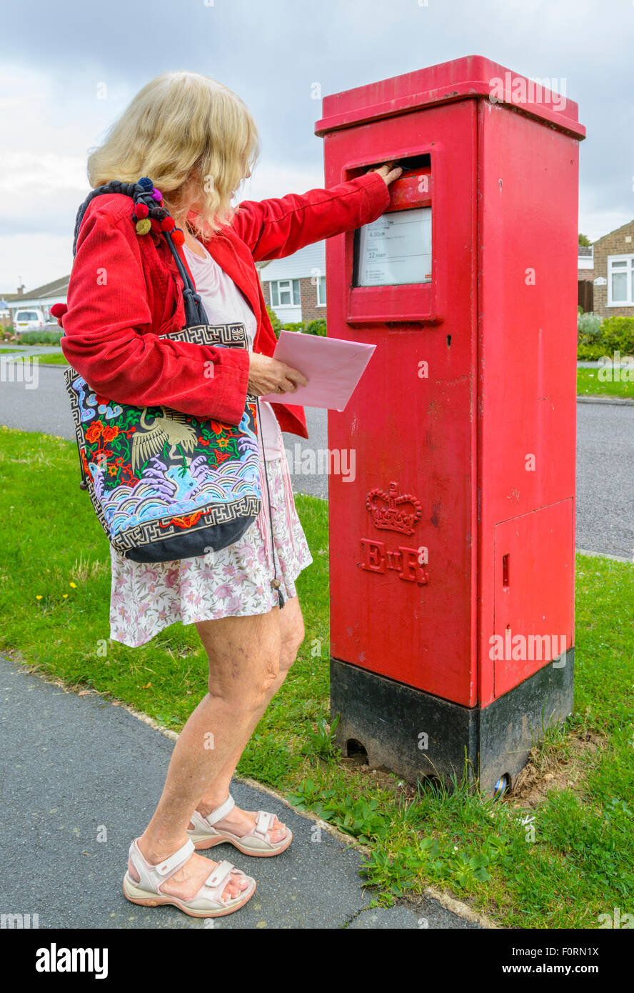 Applying Frau Entsendung einen Brief in einen roten rechteckigen Briefkasten in England, UK. Stockfoto
