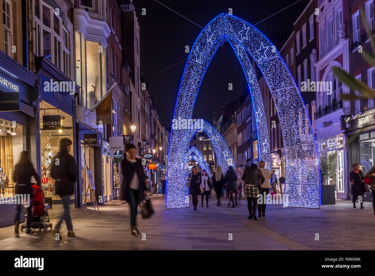 Menschen, die zur Weihnachtszeit an der South Moulton St entlang gehen, die mit großen blauen Weihnachtsbögen geschmückt ist, London, Großbritannien Stockfoto