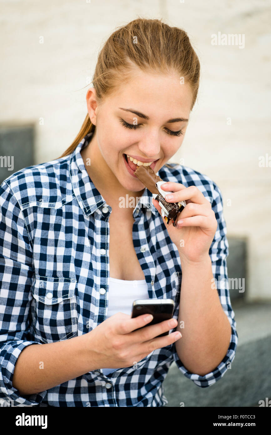 Teenager - Mädchen Schokolade zu essen, in der Straße und auf der Suche im Telefon Stockfoto