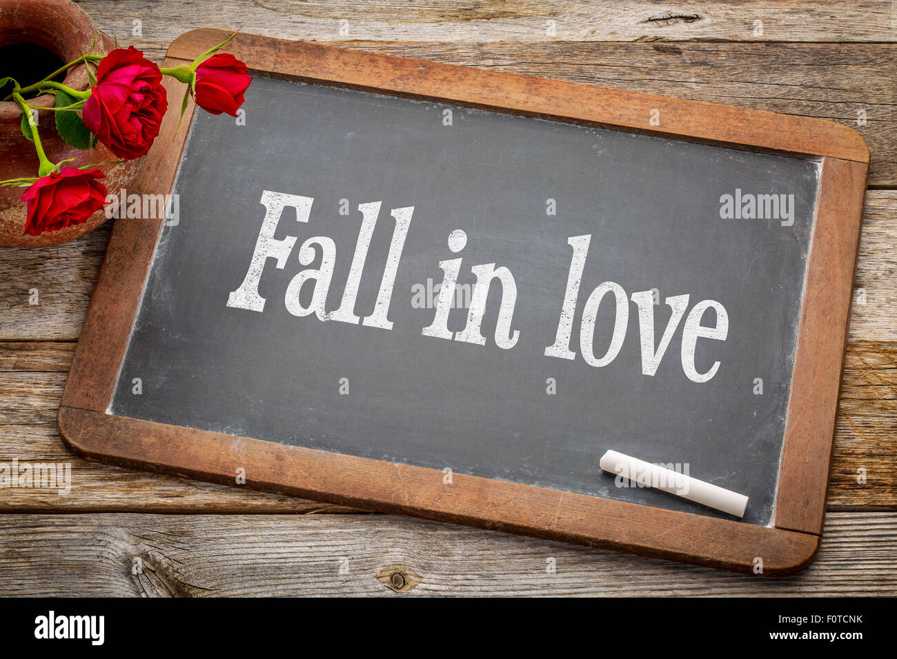 Verlieben Sie sich in Liebe Beratung - weiße Kreide Text auf einer Vintage Schiefer-Tafel mit roten Rosen gegen rustikale Holz Stockfoto