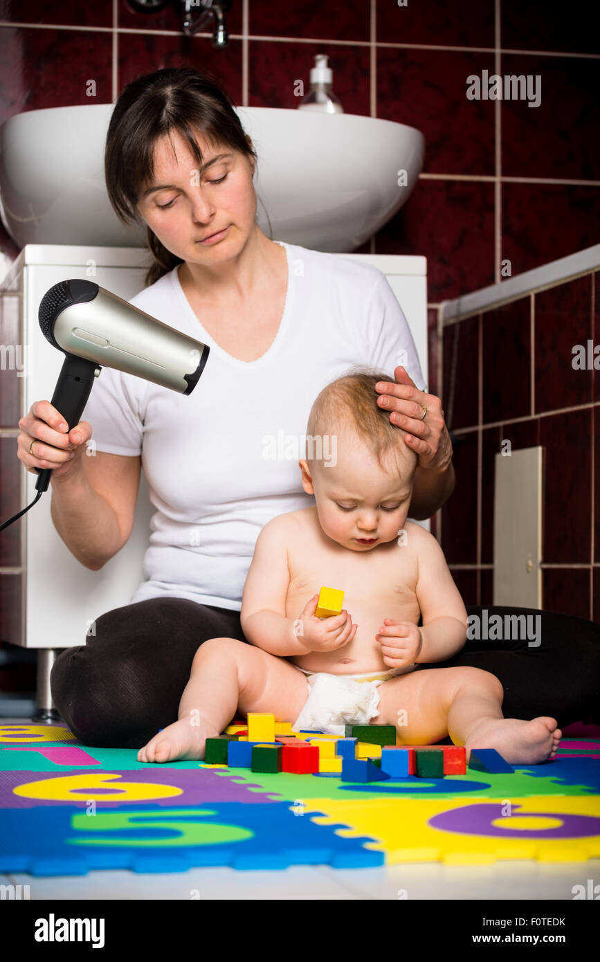 Mutter trocknen Haare ihres Kindes während Baby mit Spielzeug spielt Stockfoto