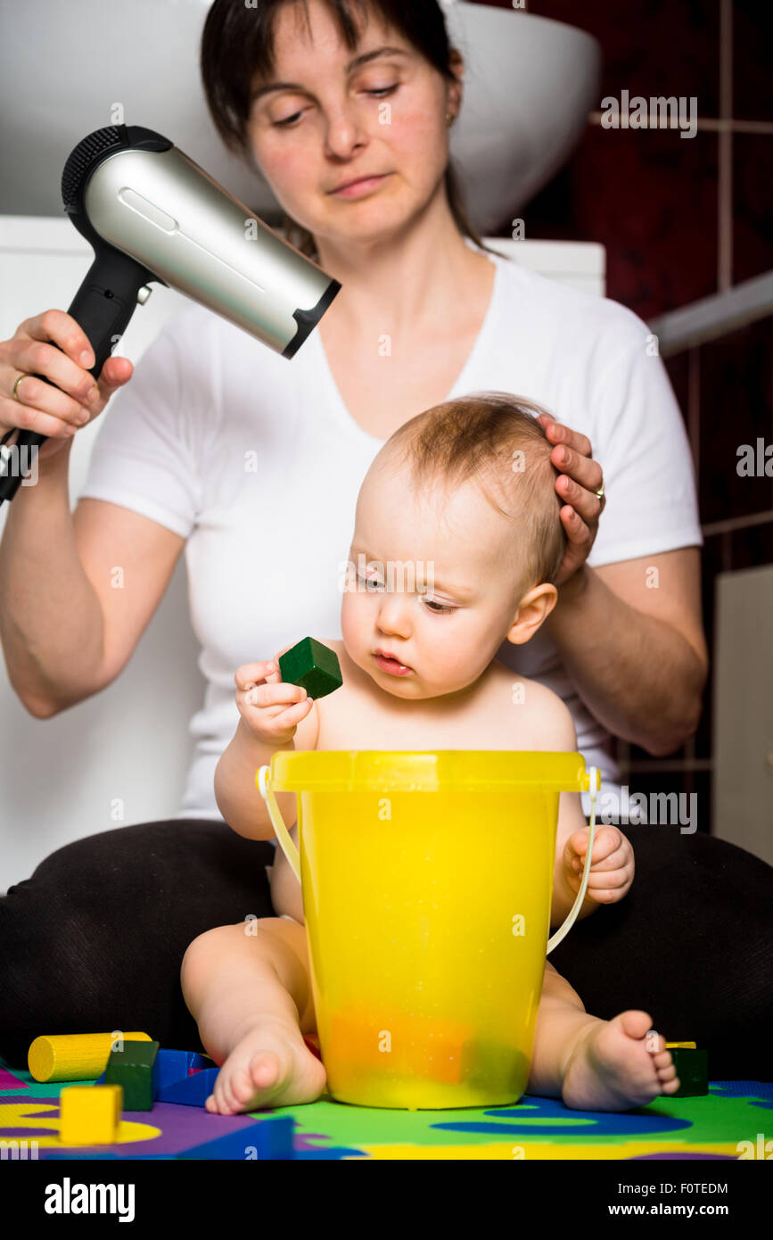 Mutter trocknen Haare ihres Kindes während Baby mit Spielzeug spielt Stockfoto