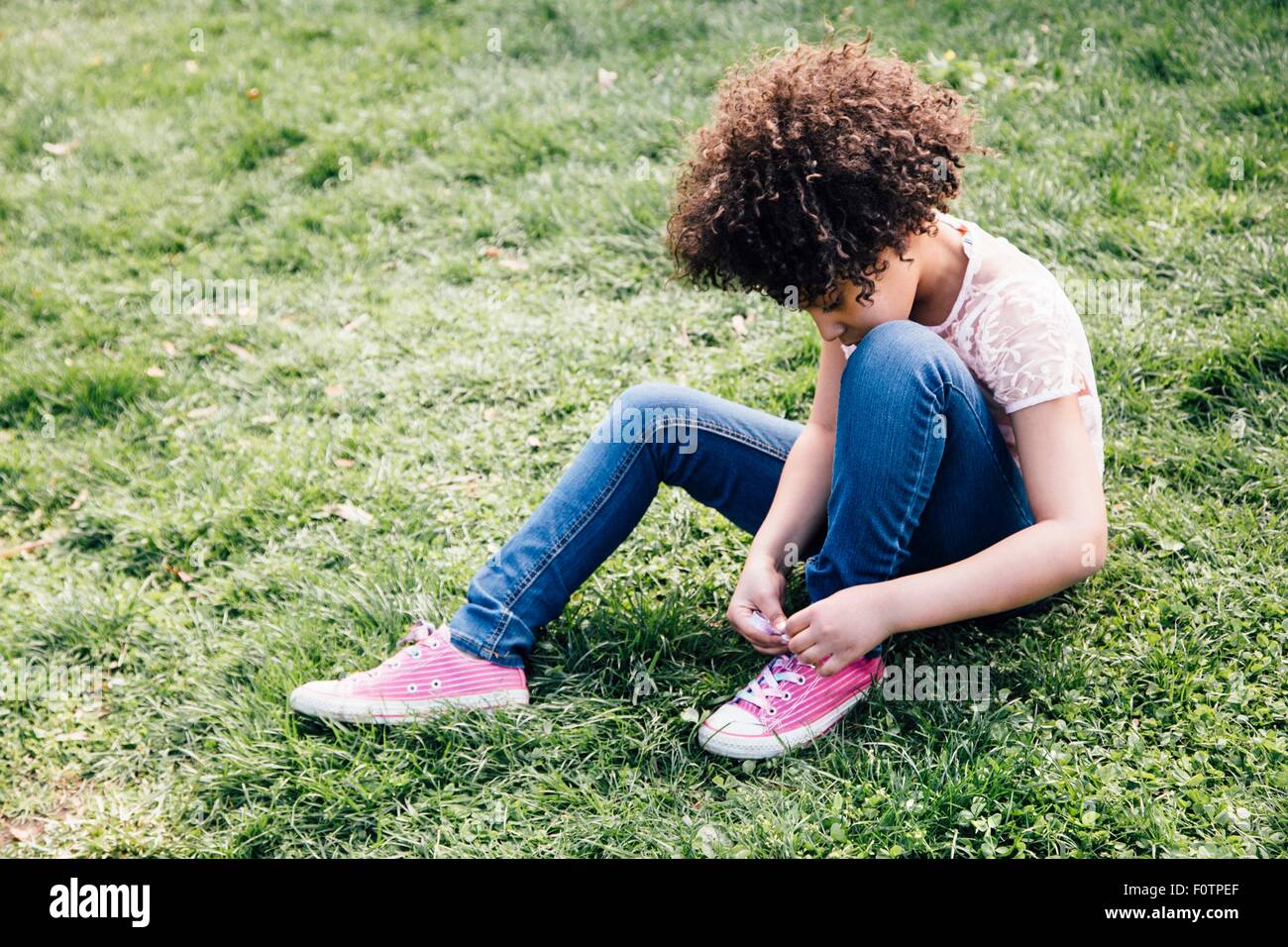Mädchen mit rosa Schuhen sitzen auf Rasen binden der Schnürsenkel, Blick nach unten Stockfoto