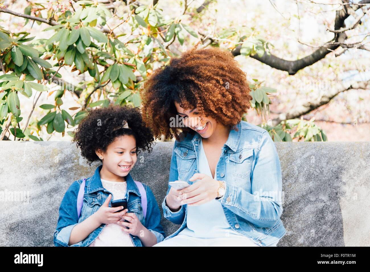 Mutter und Tochter sitzen nebeneinander mit Blick auf Smartphones zu Lächeln Stockfoto